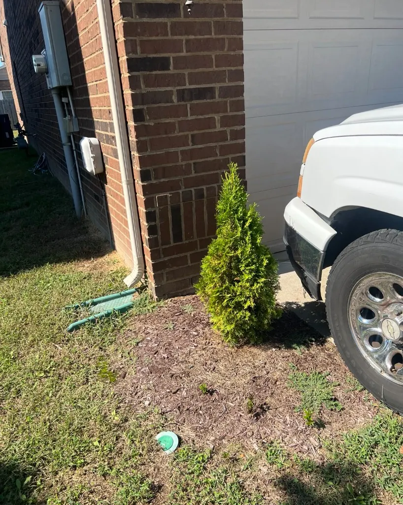 Small landscape bed beside a garage with thin mulch and a worn edge before cleanup in Brentwood