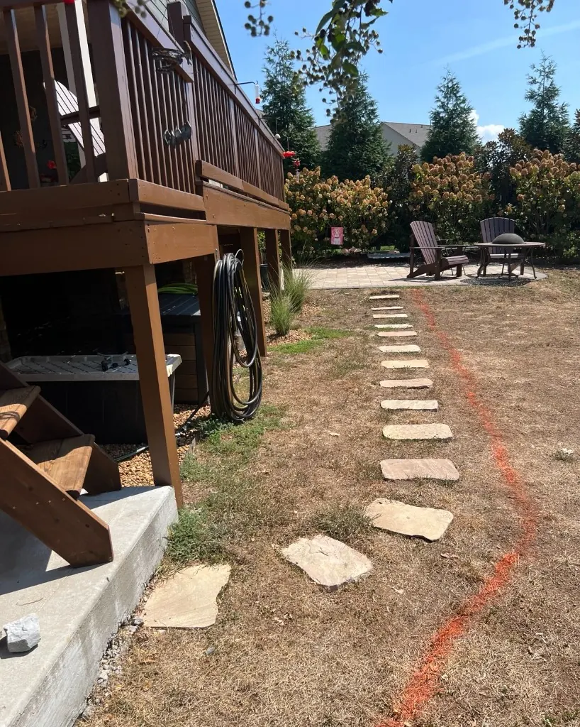 Stepping stone path beside a wooden deck marked with spray paint before pea gravel walkway installation in College Grove, Tennessee