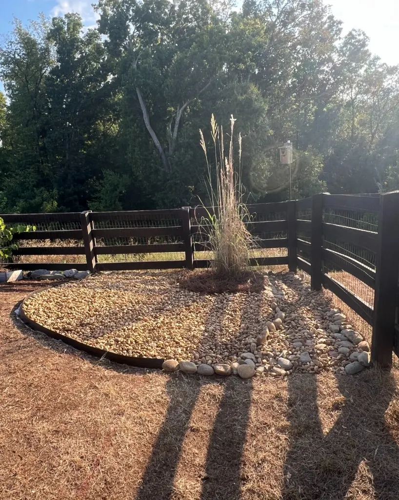 Tennessee River rock bed with landscape edging and a rock drainage swale at a fence corner in College Grove, Tennessee
