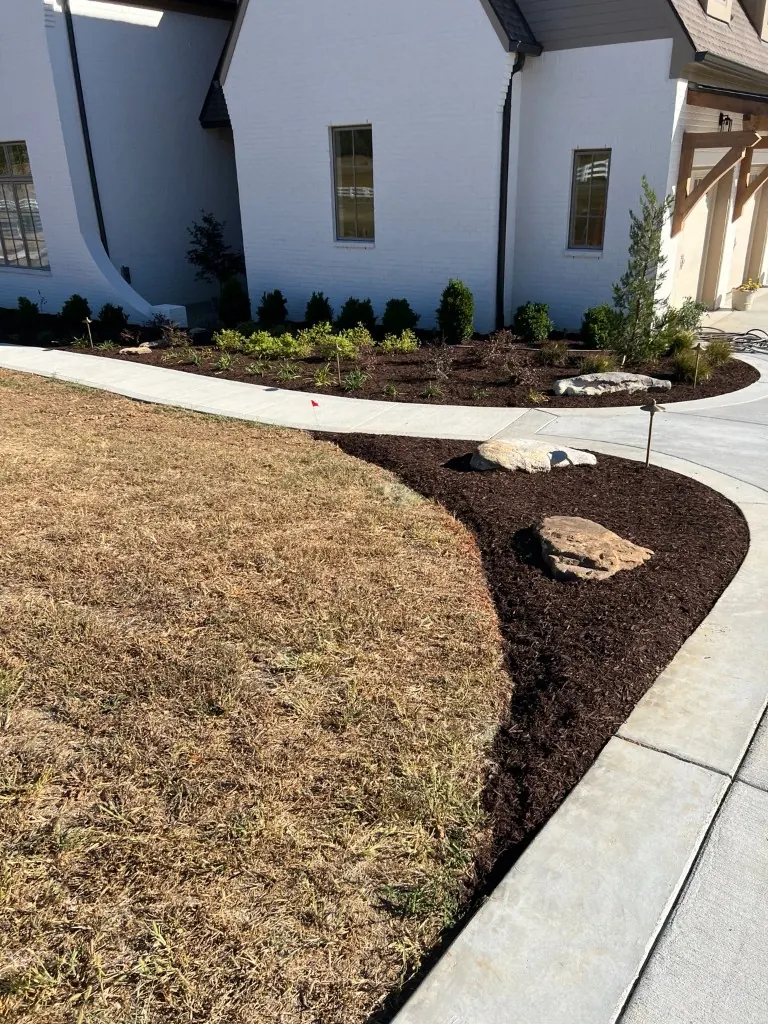 Extended front and side landscape bed with brown mulch and a large landscape boulder in College Grove, Tennessee