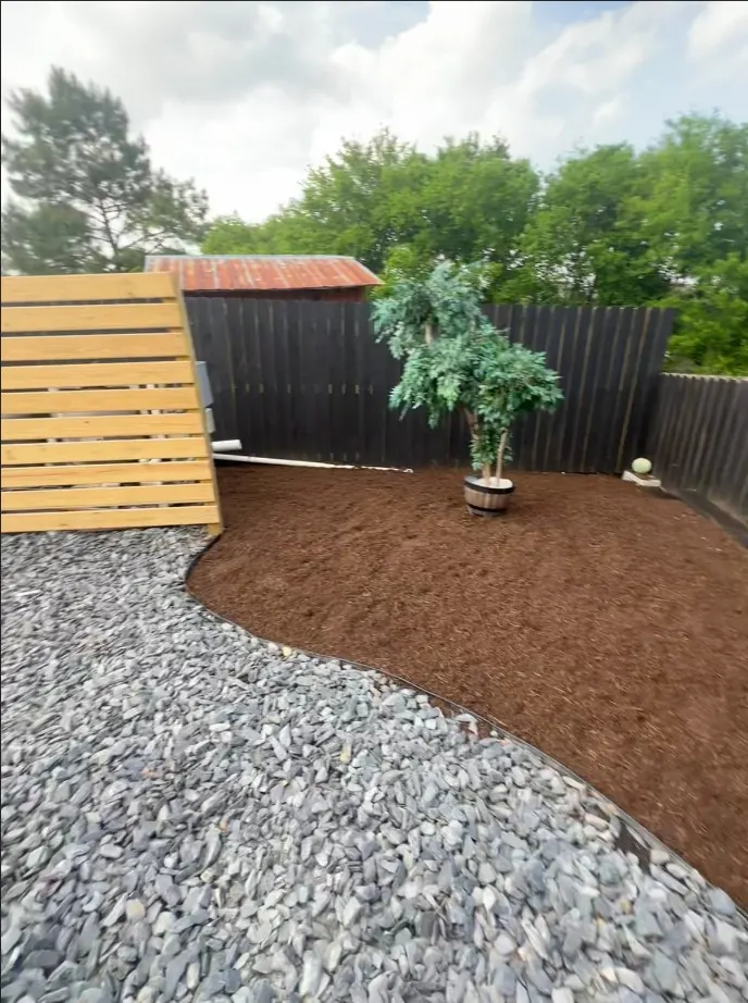 Finished mulched landscape bed with curved edging and a planted container along a privacy fence in Spring Hill, Tennessee
