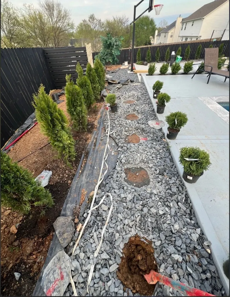 MRX Landscaping installing plants along a privacy fence with staged shrubs and active digging in Spring Hill, Tennessee