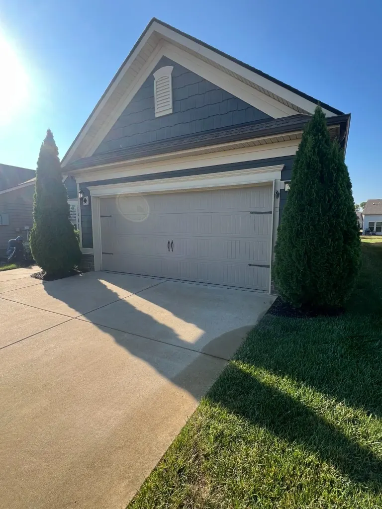 Garage flanking beds with black rubber mulch at the base of evergreen trees before rubber mulch removal in Spring Hill, Tennessee